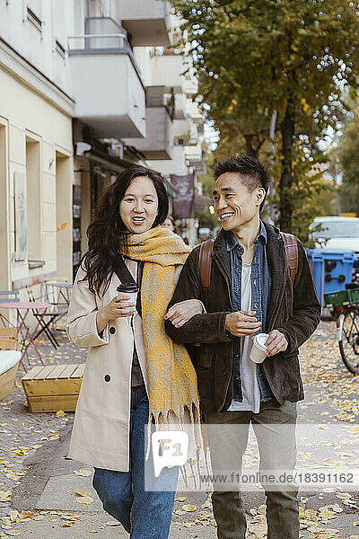 Male and female friend talking while strolling on sidewalk during autumn