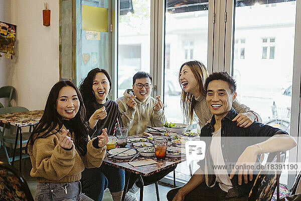 Fröhliche multirassische männliche und weibliche Freunde gestikulieren und lachen beim Mittagessen im Restaurant