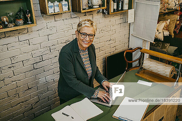 Hochwinkliges Porträt eines lächelnden älteren Unternehmers  der einen Laptop in einem Geschäft für Wohnkultur benutzt