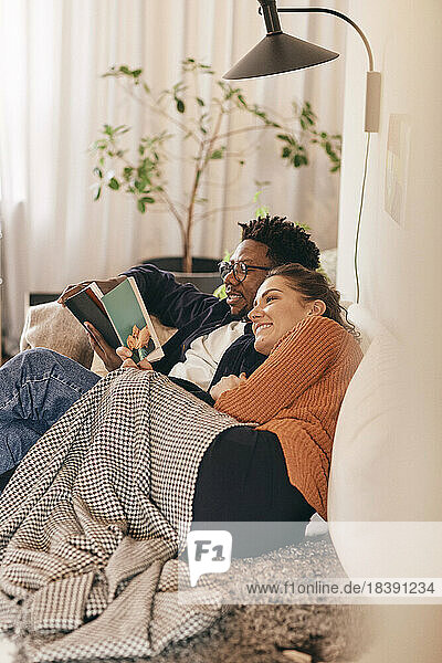 Man and woman reading books while sitting on sofa at home