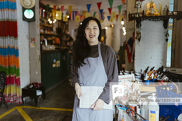 Portrait of smiling female owner holding menu card while standing at restaurant
