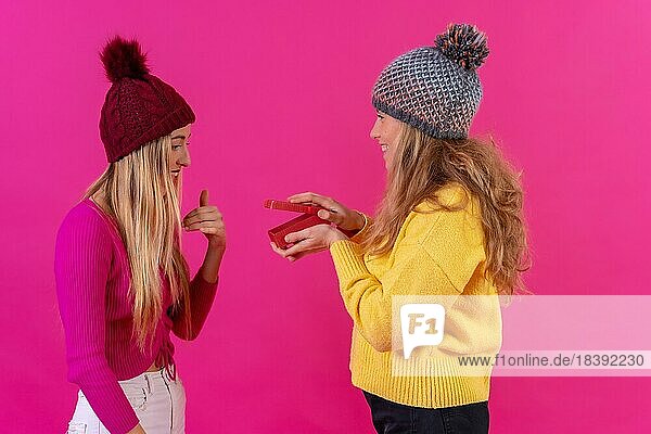 Zwei junge blonde kaukasische Frauen geben ein Geschenk in einer isolierten auf einem rosa Hintergrund