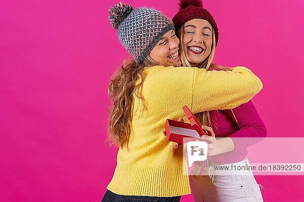 Zwei junge blonde kaukasische Frauen umarmen die Freundin und danken ihr für das Geschenk  vor einem rosa Hintergrund