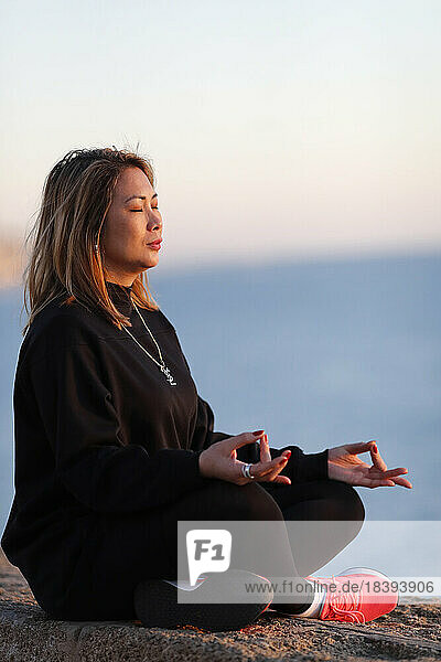 Frau bei einer Yoga-Meditation am Meer vor Sonnenuntergang als Konzept für Ruhe  Harmonie und Entspannung  Spanien  Europa