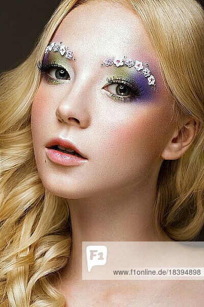 Schöne junge blonde Frau mit kreativen Make up Farbe  Locken und Blumen auf Augenbrauen. Schönheit Gesicht. Kunst Make up. Fotos im Studio geschossen