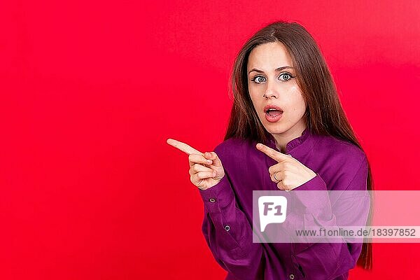 Attraktive Frau lächelnd zeigt mit den Fingern auf den Kopierraum auf rotem Hintergrund  lila Hemd