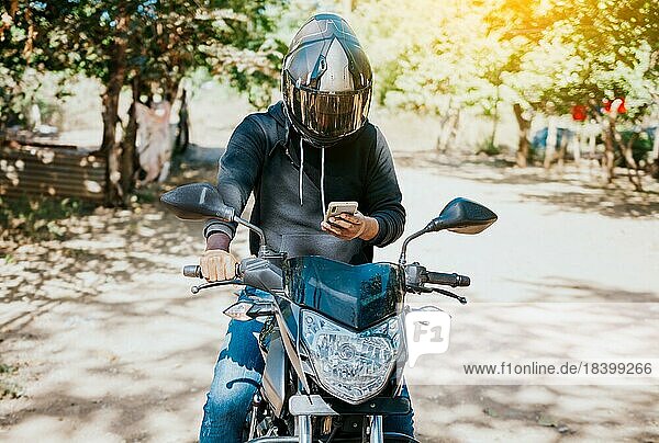 Mann auf Motorrad  der während der Fahrt eine SMS schreibt. Motorradfahrer auf Motorrad mit Handy im Freien. Konzept eines abgelenkten Motorradfahrers mit Mobiltelefon