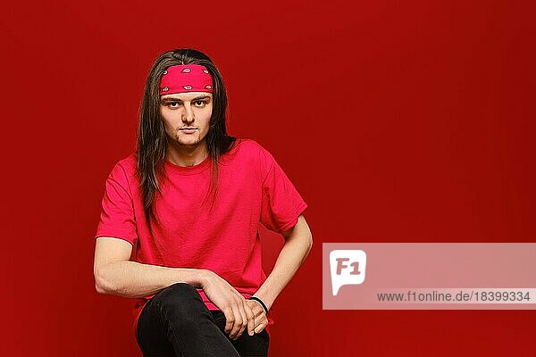 Studioporträt eines selbstbewussten jungen Mannes mit rotem Stirnband und Hemd