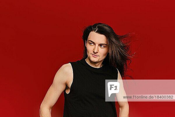 Studio portrait of young handsome man with waiving long hair on red background