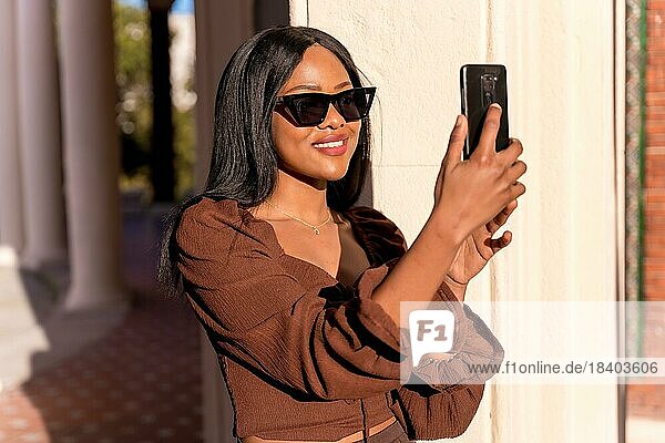 Eine schöne natürliche junge afrikanische Frau in einem Park. Mit Sonnenbrille und Blick auf das Telefon