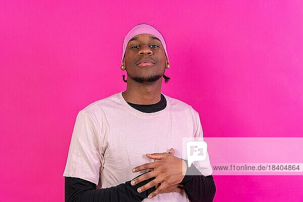 Schwarzer ethnischer Mann in rosa Kleidung auf rosa Hintergrund  Konzeptporträt  verschränkte Arme
