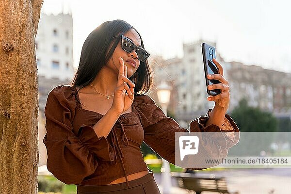 Eine schöne natürliche junge afrikanische Frau in einem Park. Mit Sonnenbrille und Blick auf das Telefon bei Sonnenuntergang