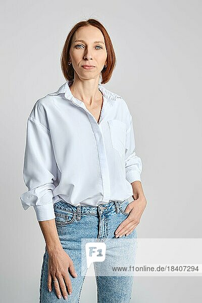 Portrait of confident middle aged woman posing against grey studio background