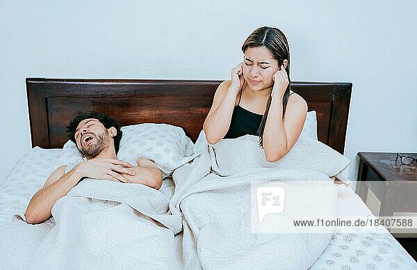Ehemann schnarcht  während die Frau leidet und sich die Ohren zuhält. Schlafapnoe Konzept  Schnarchender Mann im Schlafzimmer und Frau hält sich die Ohren zu