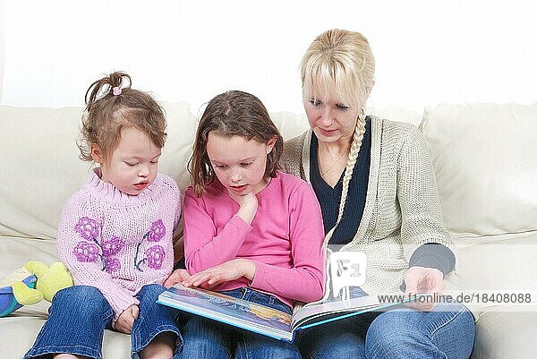 Mutter und Kinder sitzen im Wohnzimmer und lesen ein Buch