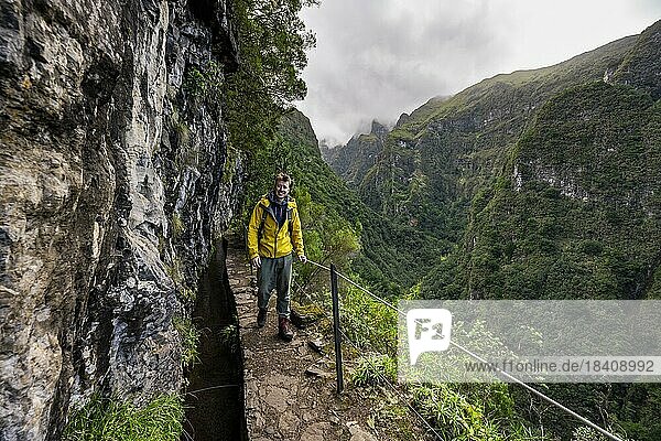Hikers on a narrow path along a levada  view of forested mountains and gorges  Levada do Caldeirão Verde  Parque Florestal das Queimadas  Madeira  Portugal  Europe
