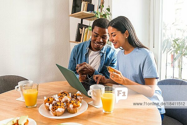 Ein Paar kauft online am Computer ein  während es frühstückt  neben dem Fenster  um Flüge zu kaufen
