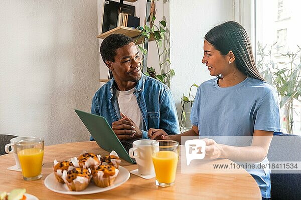 Multiethnisches Paar  das beim Frühstück mit dem Computer online einkauft  neben dem Fenster