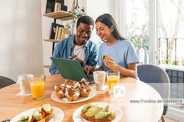 Couple making purchase online with the computer while having breakfast  next to the window  booking the holidays