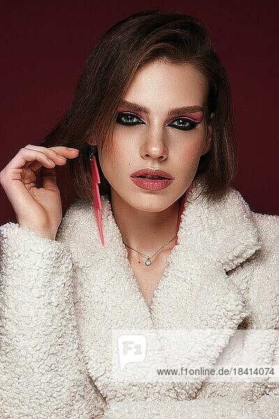 Eine schöne junge Frau in einem weißen Pelzmantel mit hellrosa Make up und Ohrringen. Schönes Gesicht. Foto im Studio aufgenommen