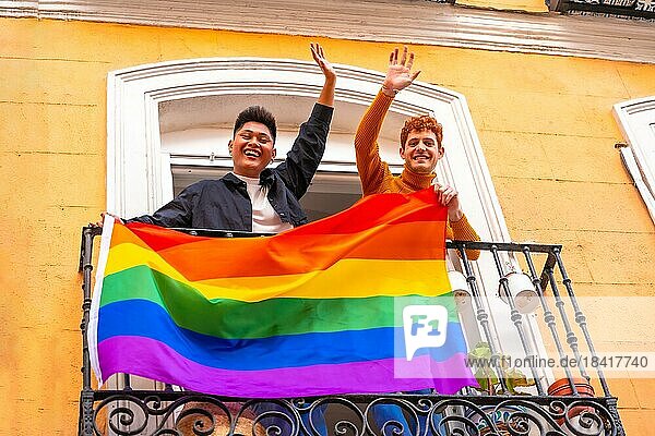 Homosexuell Junge Paare mit lgbt Flagge auf Balkon zu Hause Partei  winken lächelnd  LGBT Stolz