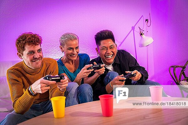 Gruppe junger Freunde  die zusammen auf dem Sofa zu Hause Videospiele spielen  lilafarben  die Spaß haben