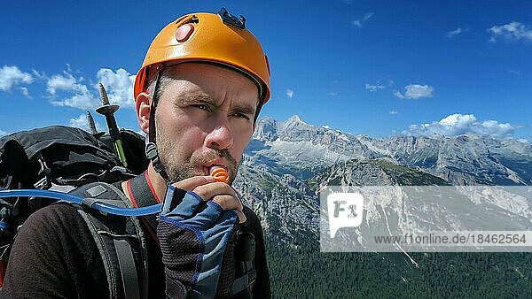 Ein durstiger Tourist trinkt Wasser durch einen Schlauch vor dem Hintergrund eines beeindruckenden Bergpanoramas in den Dolomiten. Dolomiten  Italien  Dolomiten  Italien  Europa