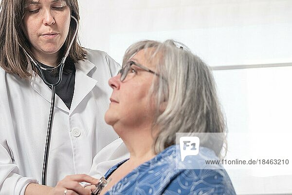 Junge Ärztin  die mit ihrem Stethoskop einen Patienten abhört  vor einem weißen Hintergrund