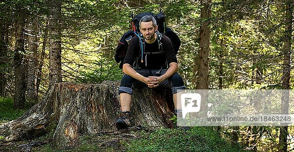A man sitting with a backpack on a tree trunk by the trail. Dolomites  Italy  Dolomites  Italy  Europe