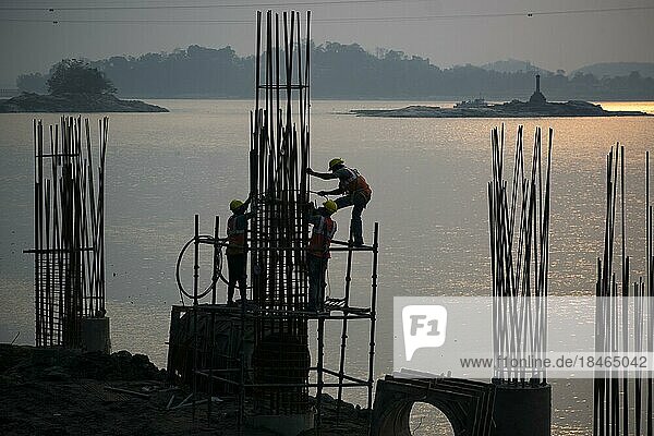 Guwahati  Indien. 27. März 2023. Bauarbeiter bei der Herstellung von Betonmasten in der Nähe des Brahmaputraflusses während des Sonnenuntergangs in Guwahati