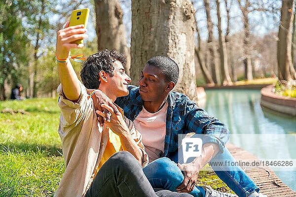 Selfie of a multiethnic gay male couple talking in the park by a river  lgbt concept