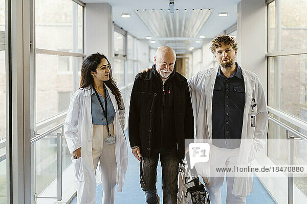 Lächelnde Ärztin  die an einem Kollegen mit einem Patienten in einem Krankenhausflur vorbeigeht