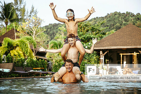 Glücklicher Vater  der seine Kinder auf den Schultern trägt  während er sich im Schwimmbad vergnügt