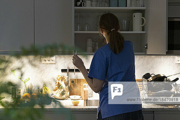 Rückansicht einer Krankenschwester  die Gläser aus einem Schrank in der Küche zu Hause entfernt