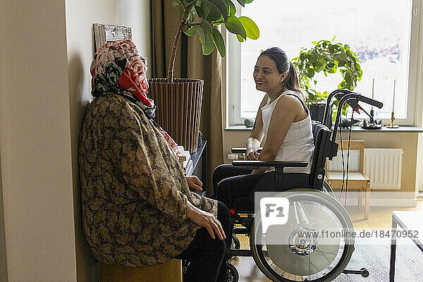 Seitenansicht einer querschnittsgelähmten Frau im Gespräch mit ihrer Mutter zu Hause