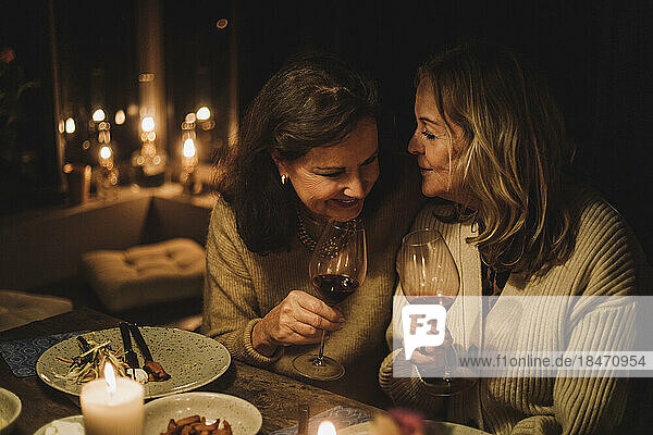 Ältere Freundinnen unterhalten sich und halten Weingläser während einer Dinnerparty bei Kerzenschein