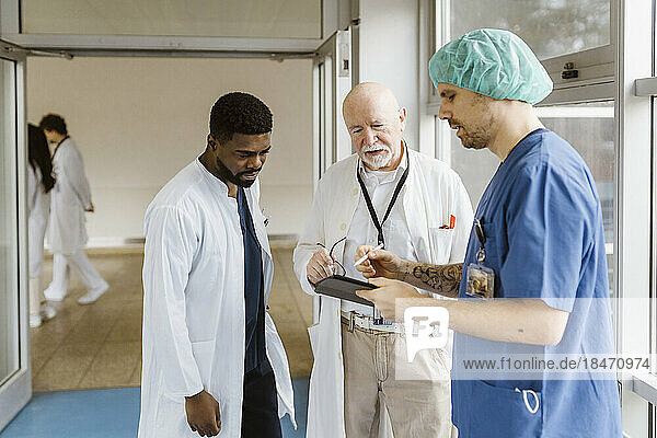 Arzt und Ärzte diskutieren über ein digitales Tablet  während sie im Flur eines Krankenhauses stehen