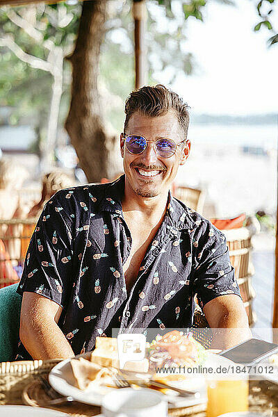 Porträt eines lächelnden Mannes mit Frühstück auf dem Tisch in einem Resort an einem sonnigen Tag
