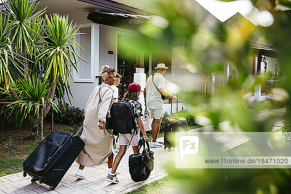 Familie mit Gepäck auf Rädern auf dem Fußweg bei der Ankunft am Urlaubsort