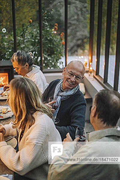 Smiling senior man talking to retired male friend during dinner party