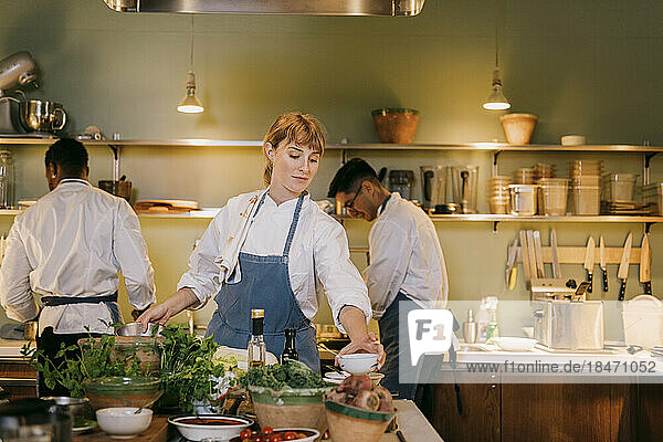 Junge Köchin bei der Zubereitung von Speisen mit Kollegen in einer Großküche