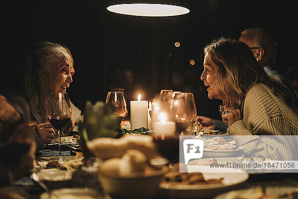 Ältere Frau im Gespräch mit einer Freundin am Esstisch während eines Abendessens bei Kerzenschein