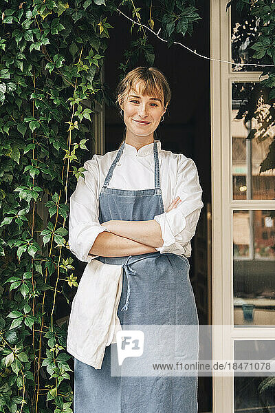Portrait of smiling female chef standing with arms crossed outside restaurant