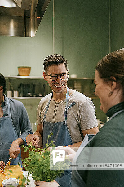 Glücklicher männlicher Student im Gespräch mit einer Freundin während eines Kochkurses in der Küche