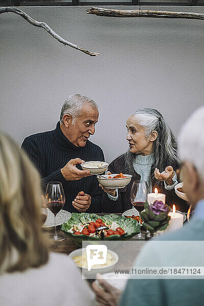 Männliche und weibliche Freunde halten Essensschalen  während sie sich auf einer Dinnerparty unterhalten