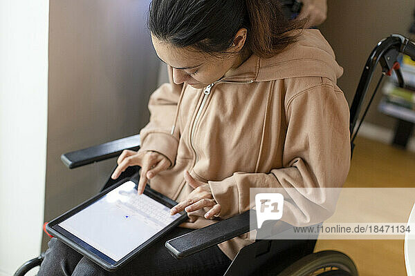 High angle view of woman with paraplegia using tablet PC while sitting on wheelchair at home