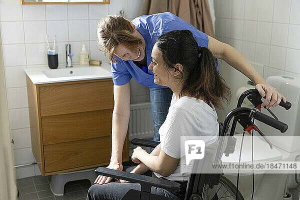 Glückliche Pflegerin im Gespräch mit einer querschnittsgelähmten Frau im häuslichen Badezimmer