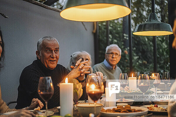 Reifer Mann mit verschränkten Händen  der mit männlichen und weiblichen Freunden auf einer Dinnerparty sitzt