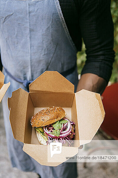Hoher Blickwinkel eines männlichen Restaurantbesitzers  der einen frisch zubereiteten Burger in einer Schachtel hält