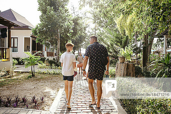 Rückansicht eines Vaters  der mit seinem Sohn auf dem Fußweg bei den Bungalows spazieren geht  während der Ferien